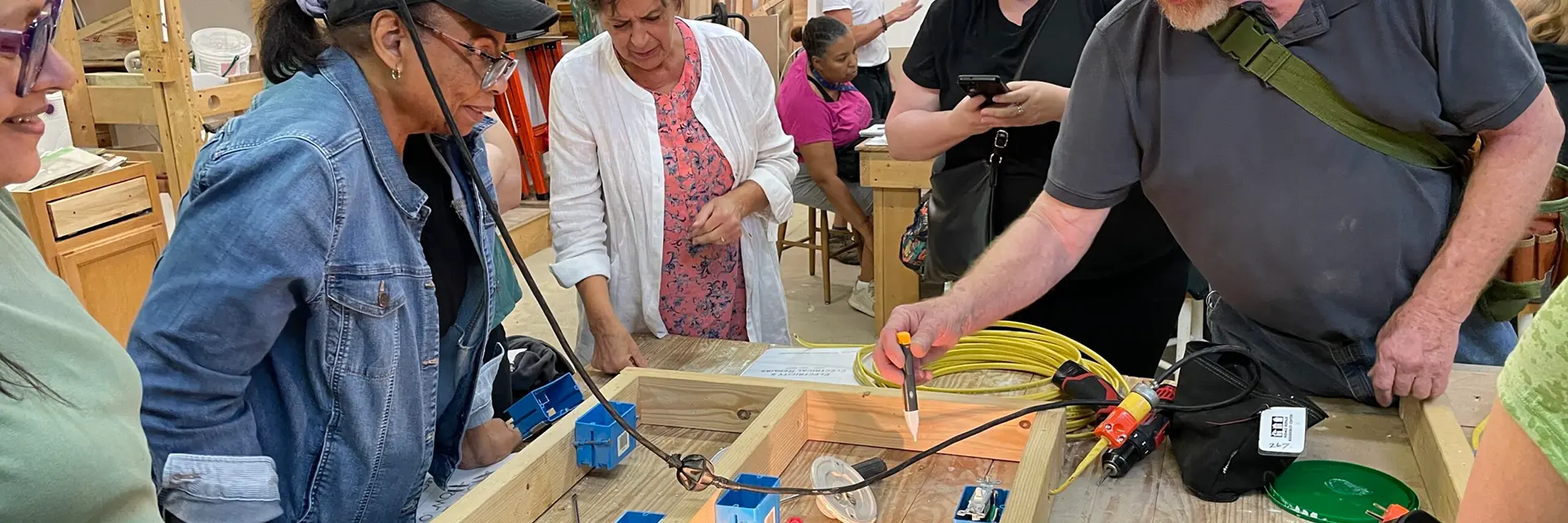 A class instructor demonstrating the use of a voltmeter on household wiring as students watch